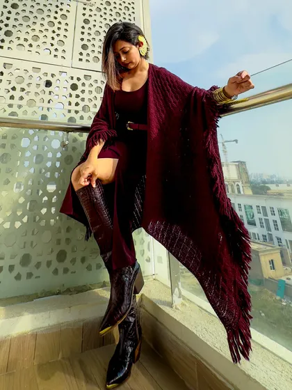 Embracing the color of the season: burgundy. This maximalist look features a monochromatic outfit with a poncho, a slit skirt, and tall boots for a dramatic, editorial feel.