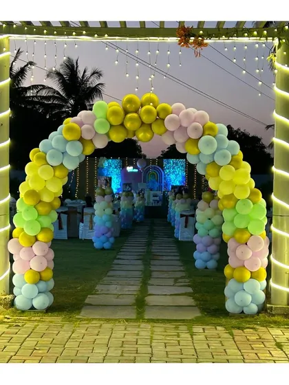 A breathtaking pastel rainbow balloon archway creating a grand entrance for an outdoor event. This welcoming decor piece, illuminated by string lights, sets a joyful and celebratory tone from the moment guests arrive.