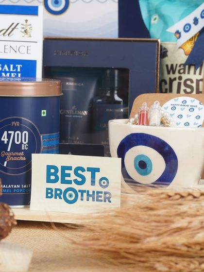 This shot highlights the premium items in the 'Shielded in Blue' hamper. It includes a men's grooming set from Kimirica, gourmet popcorn from 4700BC, and a 'Best Brother' card, showing that a Rakhi gift can be both traditional and luxurious.