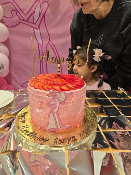 A closer look at the custom Pink Panther birthday cake, complete with a personalized topper and fresh strawberries, just before the candles are lit.