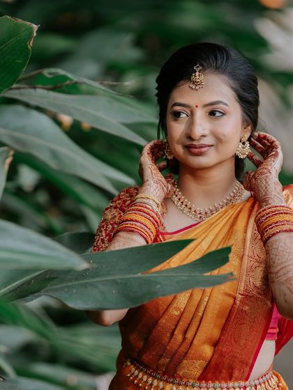 Elegance in every detail. This bride's soft glam makeup, with its subtle shimmer and defined eyes, is the perfect accompaniment to her vibrant yellow-orange saree and intricately embroidered blouse.