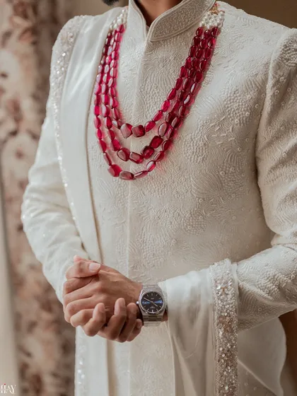 A close-up on the details of the groom's attire, from his textured white sherwani to his layered ruby necklace.