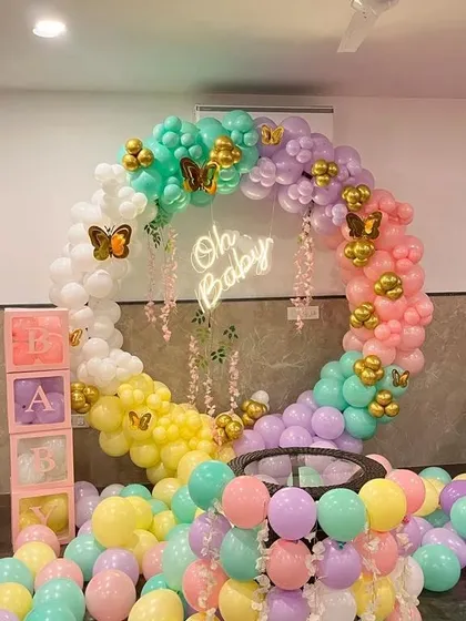 A whimsical butterfly-themed baby shower setup. This design features a full ring arch decorated with a rainbow of pastel balloons, gold butterfly accents, an 'Oh Baby' neon sign, and 'BABY' blocks, creating a magical and photo-ready scene.