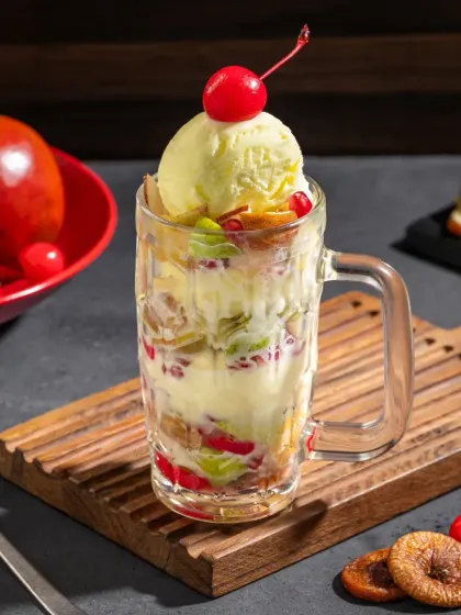 A fruit and nut sundae in a glass mug, packed with fresh fruits like apple, pomegranate, and figs.