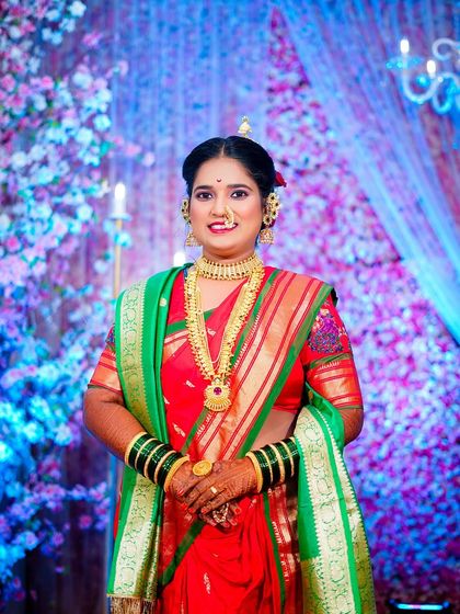 A classic portrait of a Maharashtrian bride in a red and green saree. She is adorned with traditional gold jewellery, including a long necklace and nath, against a festive floral background. (Duplicate of 61)