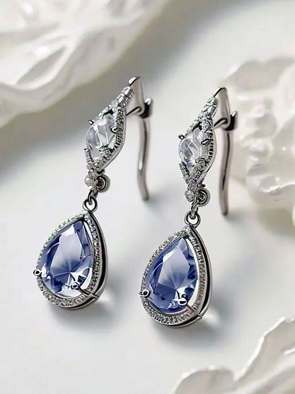 A stunning macro shot of blue gemstone and diamond drop earrings against a white, textured background. For jewelry, I focus on capturing the sparkle of the stones and the intricate metalwork.