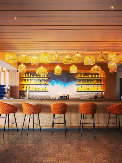 A cozy bar counter design at our recently completed project, 'Sloshed.' The warm glow of the cane pendant lights and the rich orange of the bar stools create an inviting and stylish focal point.
