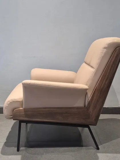 The side profile of the 'Enigma' chair highlights its distinctive dark wood frame that contrasts beautifully with the light-colored upholstery.