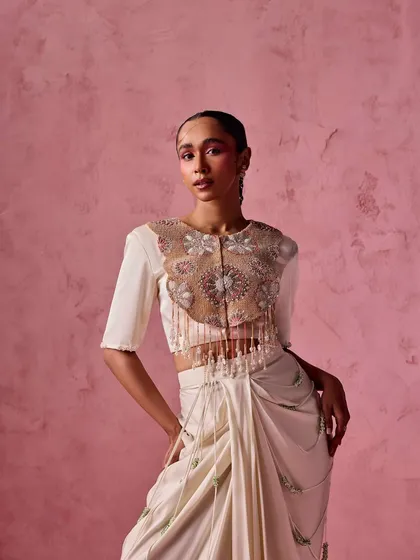 A model in an ivory draped skirt paired with a stunning crop top featuring a sheer, embroidered yoke with tassel details.