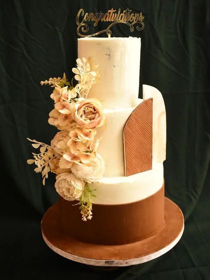 This sophisticated three-tier cake combines modern and classic elements. The design features a rich brown bottom tier, a textured middle tier with a unique wooden-panel accent, and a clean top tier, all brought together with a cascade of blush-toned flowers.