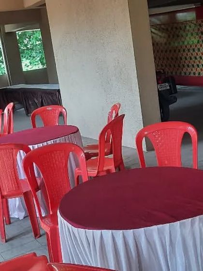Round tables with covers and red plastic chairs set up in a building's parking area. I can turn unconventional spaces into functional event venues.
