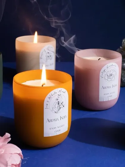 A collection of our frosted glass candles, their flames dancing among flowers. These luxury candles are designed to create a multi-sensory experience that helps you unwind, relax, and enjoy the moment.