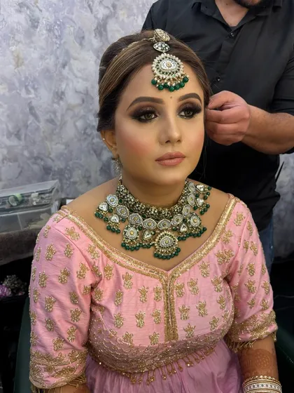 A behind-the-scenes moment of a bride getting her hair styled. Her makeup is already complete, featuring a bold smokey eye and a flawless base, ready for the final touches.