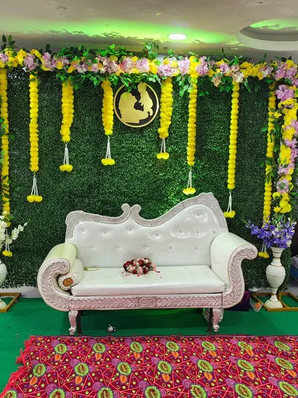 For traditional events like baby showers or naming ceremonies, I create elegant backdrops. This one uses a lush green wall, beautiful marigold garlands, and a comfortable, ornate sofa for the main seating area.