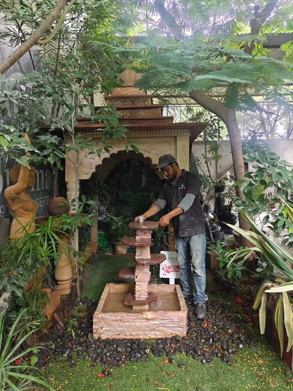 An artisan stands with the natural stone cascading fountain to show its scale. At 3 feet tall, it's a great mid-sized option for gardens.