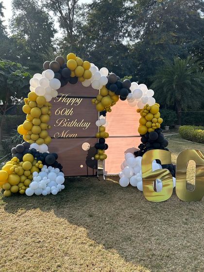 An elegant outdoor 60th birthday celebration for a client's mom. The setup features a custom backdrop with a beautiful balloon arch in mustard yellow, black, and white.