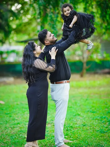 A father joyfully lifts his daughter into the air during a fun family photoshoot in the park.