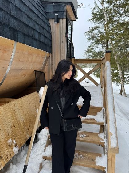 A side-profile shot of the all-black winter outfit against the snowy cabin backdrop.