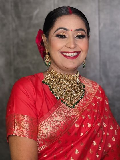 A happy reception bride in a classic red saree. Her smile is the highlight, complemented by a bold red lip and golden eye makeup.