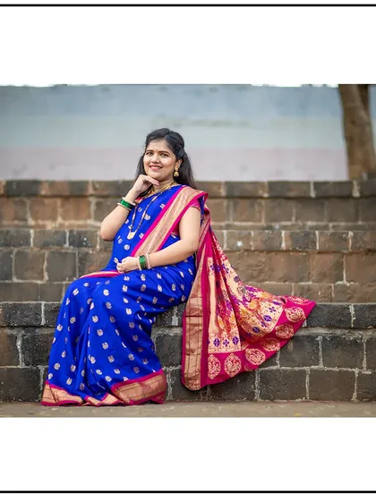 An elegant portrait of a mom-to-be in a traditional blue Paithani saree, sitting gracefully on stone steps.