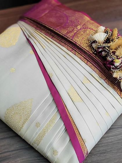 An elegant off-white bridal saree with a pink border, ready for a wedding. The box fold includes arranging the pallu with its beautiful tassels so nothing gets tangled.