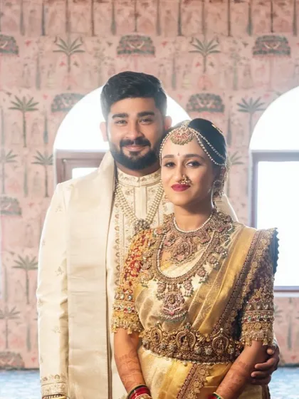 A radiant bride and groom, perfectly coordinated. Her gleaming gold saree with a rich red blouse is complemented by his elegant off white sherwani, showcasing my work in creating harmonious couple attire.