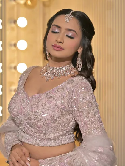 A soft glam bridal look with a pastel pink lehenga. The makeup features shimmery lilac eyeshadow and a soft pink lip, perfect for a daytime wedding or reception.