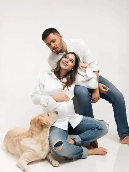 A playful moment during the maternity shoot, with the father-to-be making a funny face while their dog looks up lovingly at the baby bump.