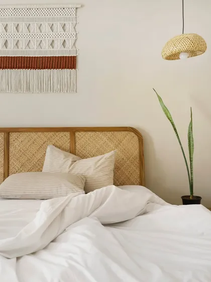 The textures of Unallome's bedroom come to life in this shot. The woven cane headboard, the soft cotton bedding, and the intricate macrame wall art create a tactile experience that is both comforting and beautiful.