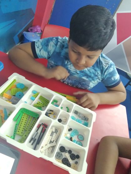 A young boy carefully selects parts from a compartmentalized VEX robotics kit for his project.