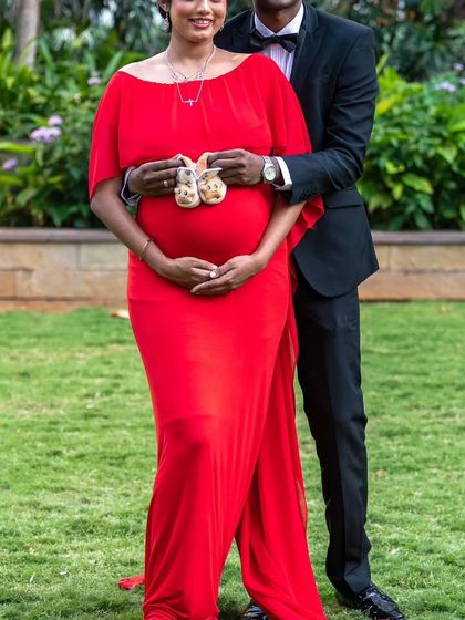 A classic couple's portrait holding tiny baby shoes. The mom-to-be's red A-line gown is a perfect, vibrant choice to celebrate this special time.