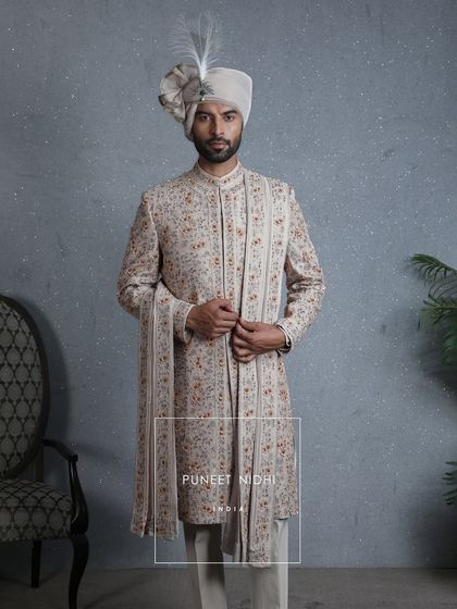 A silhouette of nobility, this coffee beige sherwani blooms with embellished floral artistry and jeweled beadwork. The lace-wrapped safa crowned with a sarpech completes its princely aura.