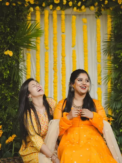 Laughter and friendship at Sanvi's Haldi ceremony. We designed this cheerful backdrop with strings of yellow marigolds and lush green leaves to create a perfect photo corner.
