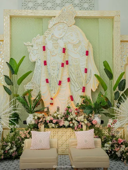 The central Radhe Krishna installation, framed by mosaic panels and adorned with a simple garland, serving as a serene and spiritual focal point for the Haldi.