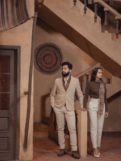 A full-length portrait of the couple in a rustic, earth-toned indoor setting, showcasing their coordinated, stylish outfits.
