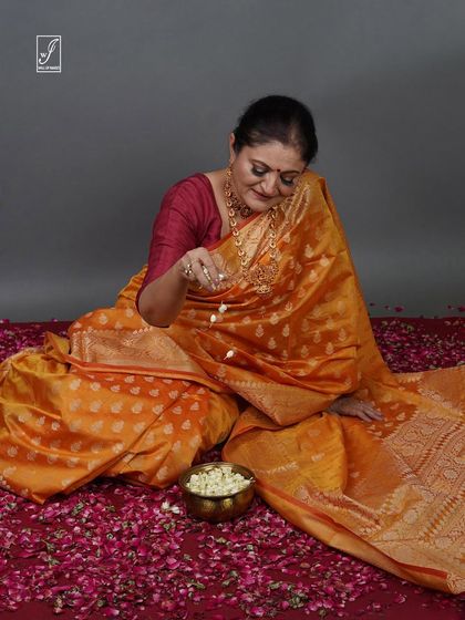A candid moment captured during a saree shoot, with the model seated amongst flower petals, creating a soft and celebratory feel.