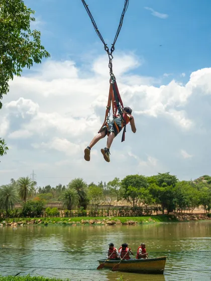 A participant flies through the air on the Superman Swing, with the lake and boats visible below.