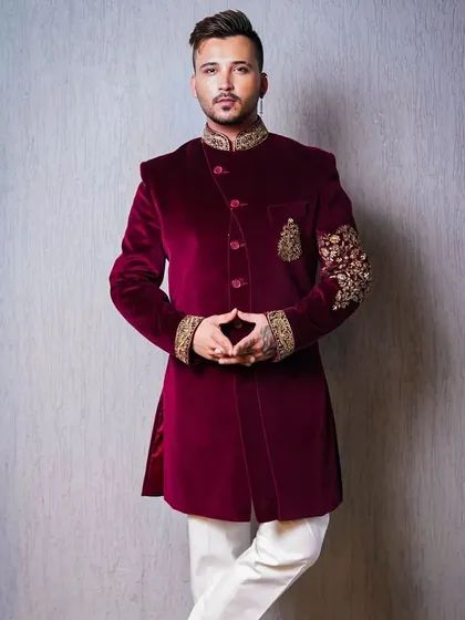 A confident pose in a modern sherwani, showcasing the exquisite gold embroidery on the sleeve and collar. This shot is designed to highlight the craftsmanship and luxurious appeal of the groom's attire.