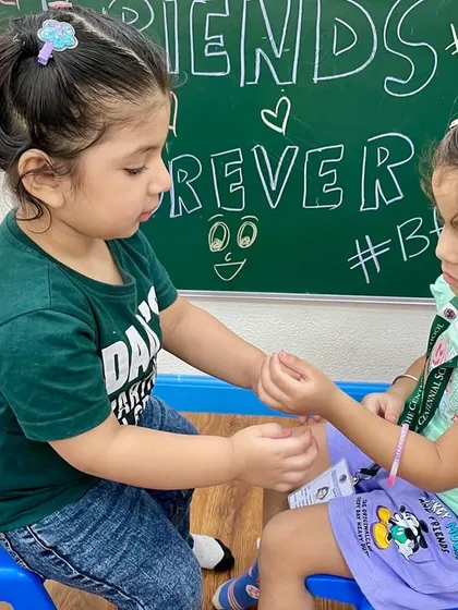 A sweet moment of friendship. One child carefully ties a friendship band on another's wrist, learning the joy of giving and sharing in a meaningful way.
