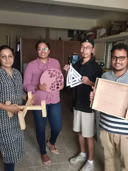 A group of students with their finished projects, including a planter stand, a decorative clock, a triangular art piece, and a wooden tray.
