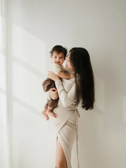 A mother holds her baby in a beautifully lit studio setting. The soft light and simple background create a timeless mother and child portrait.