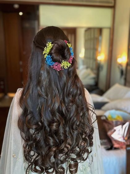 A half-up top knot surrounded by a colorful floral wreath. This is a fun and modern hairstyle for a Mehendi or Haldi, keeping the hair off the face while still looking festive.