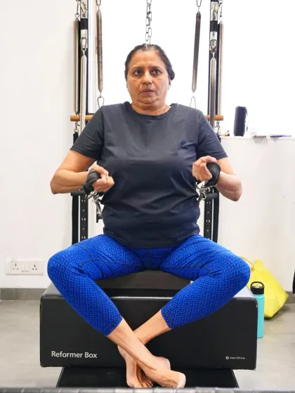 A client performs a seated row on the reformer using the reformer box. This variation is excellent for isolating the back and arm muscles while maintaining a stable, supported posture.