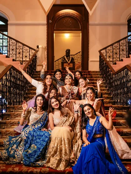 The bride and her squad sharing a laugh and waving for the camera on the grand staircase.