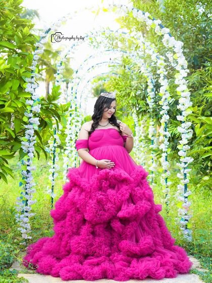 A "Barbie" themed shot with the mother-to-be in a bright pink ruffled gown and crown, standing under a floral arch.