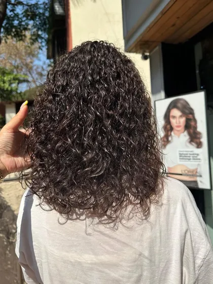 The beautiful result of a damage-free perm. These defined, bouncy curls were created using techniques that prioritize hair health, leaving the hair soft and shiny, not dry or brittle.