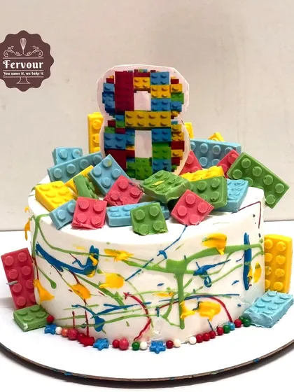 A fun Lego theme cake with zero fondant. The cake is decorated with colourful paint splatters and edible chocolate Lego blocks, making it a creative and tasty choice.