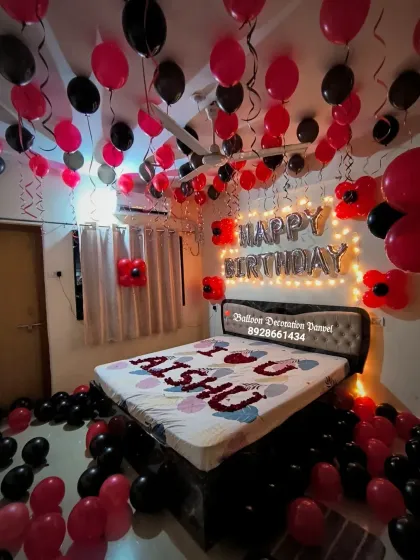 A romantic red and black themed birthday room decoration. The setup includes balloons on the ceiling and floor, and a personalized message on the bed.