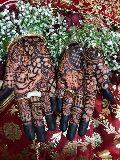 The deep, dark stain on a bride's palms, adorned with rings and fresh flowers.