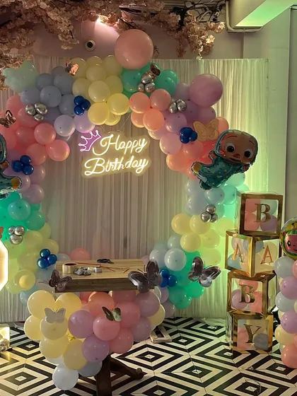 The finished Cocomelon birthday backdrop, featuring a 'Happy Birthday' neon sign, 'BABY' blocks, and character foil balloons.